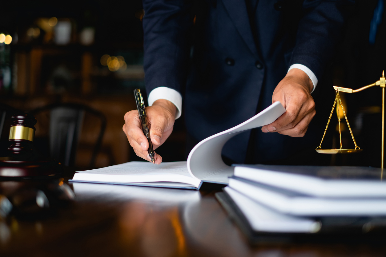Close up lawyer businessman working or reading lawbook in office workplace for consultant lawyer concept. Lawyer writing on a booklet with justice scale in the foreground