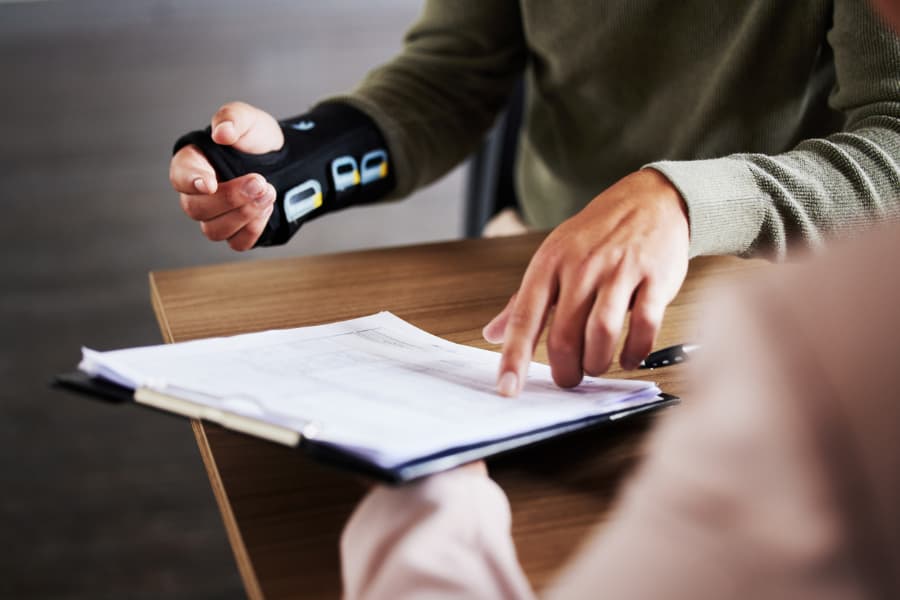 A man with a wrist brace pointing to a paper on a clipboard held by a lawyer