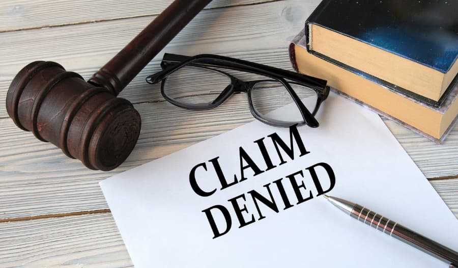 Claim denied paper with a gavel, eyeglasses and books on a desk