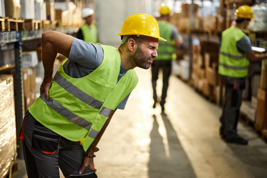Injured warehouse worker with a pained look holding his lower back