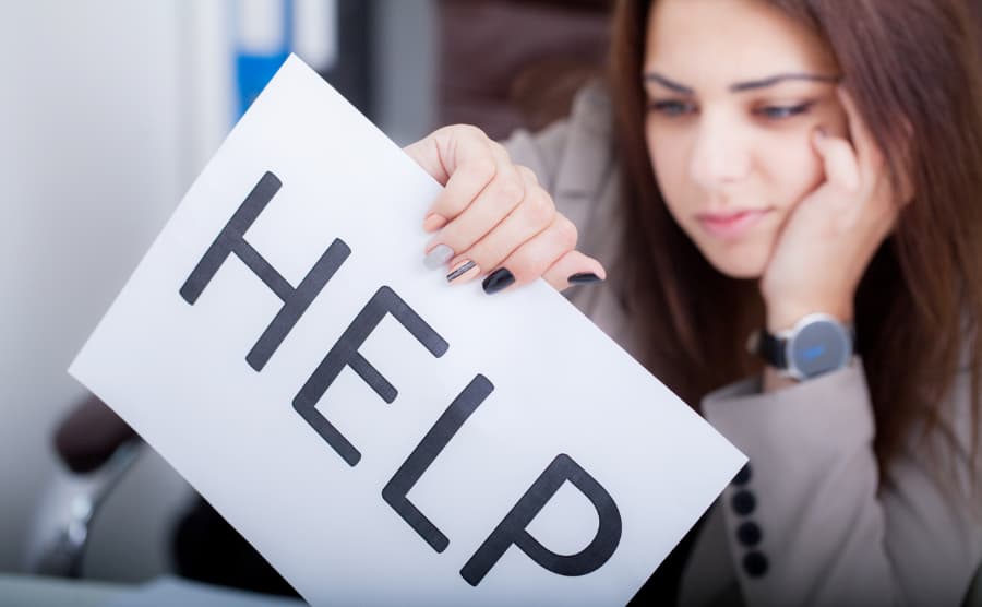 A brown haired woman with painted nails holding a sign that says help