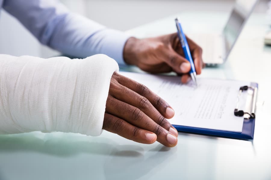 Close-up of a man’s hands holding a pen writing on an insurance form