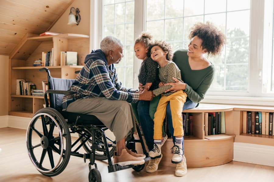 Elderly woman in a wheelchair laughing and smiling with her daughter and grandkids