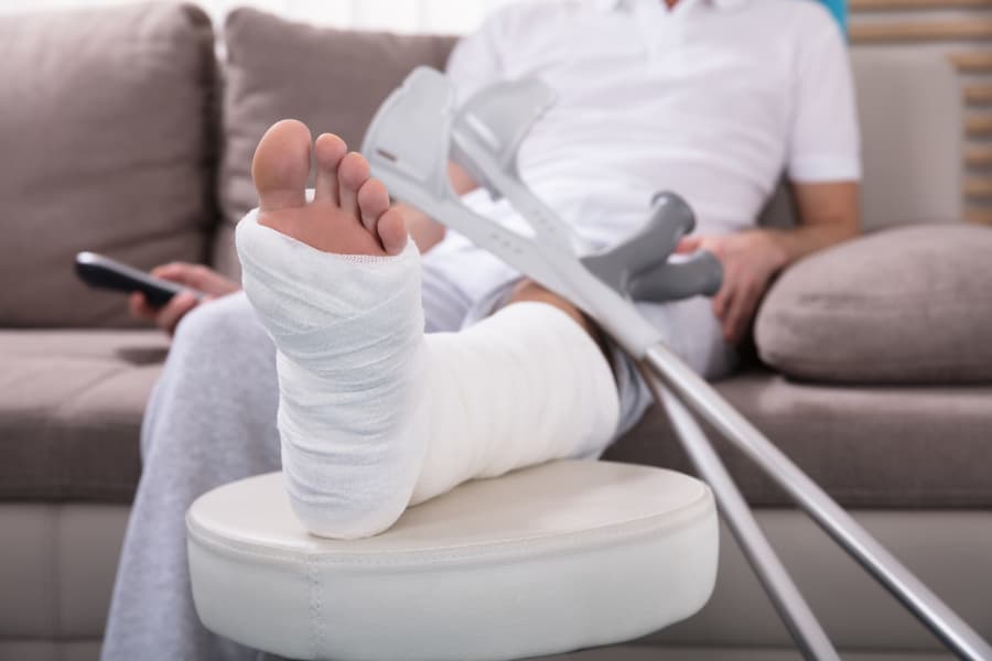 Young man with a broken leg sitting on sofa holding remote