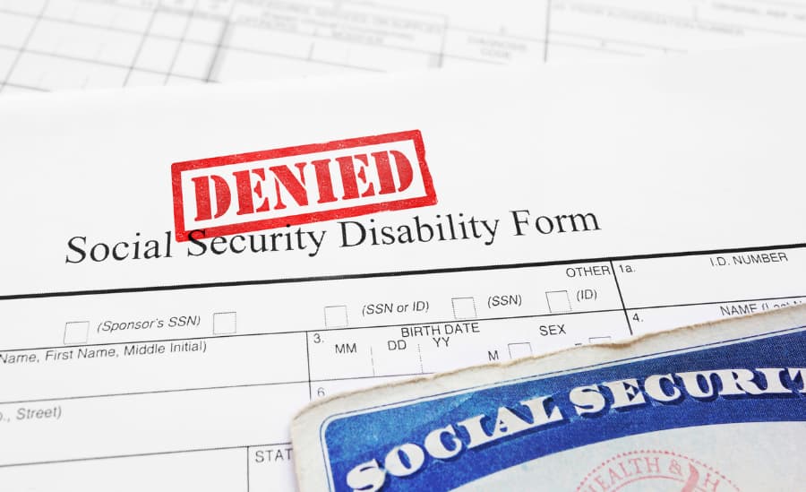 Close up of a disability claim with a denied stamp and social security card