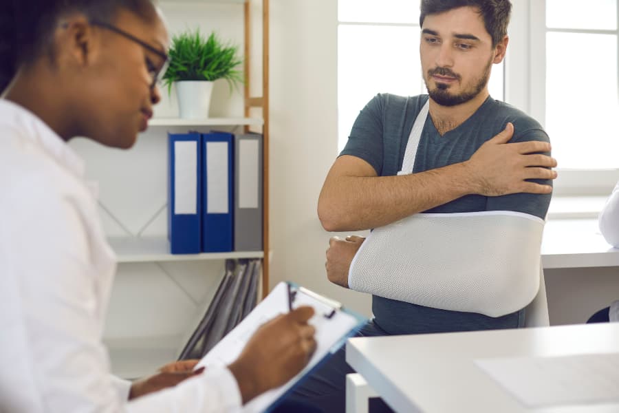 A doctor writing on a clipboard while talking to a man with his arm in a sling