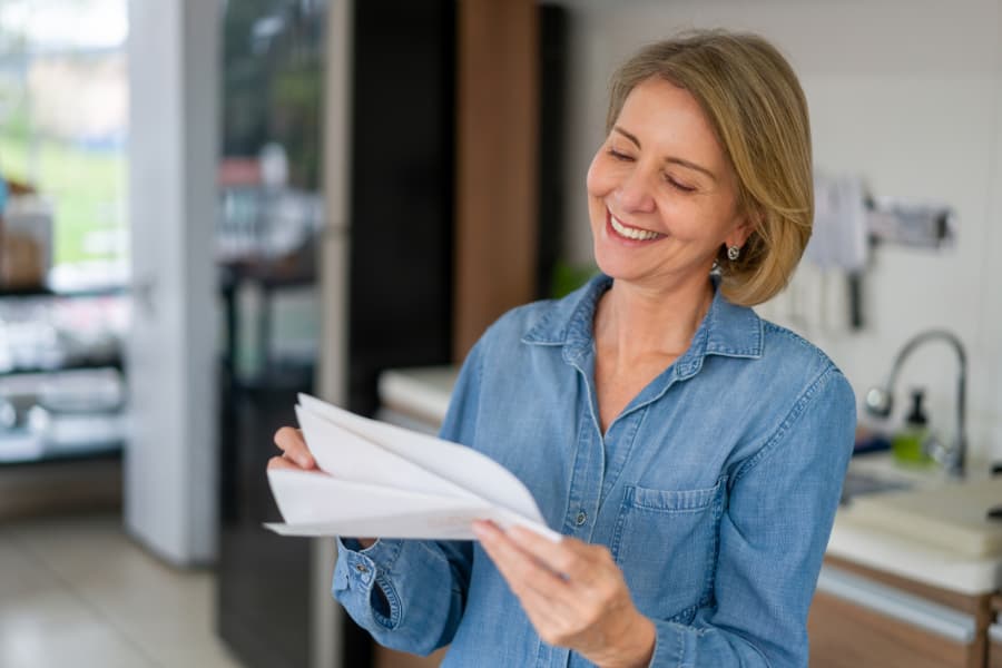 An older blond woman unfolding and reading a paper and smiling