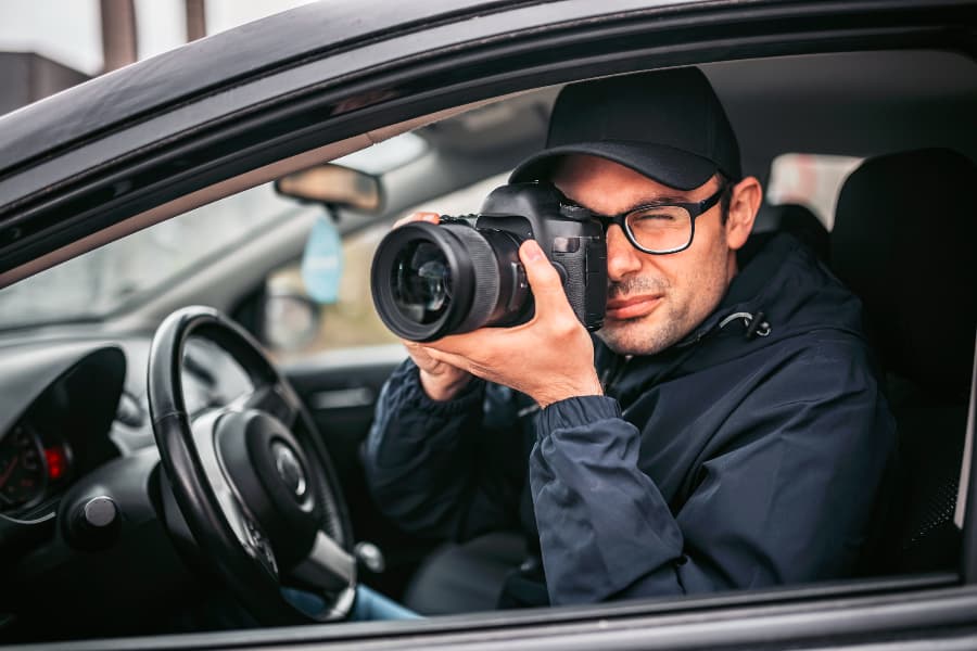 Private investigator taking photos through car window during a stake-out surveillance operation.