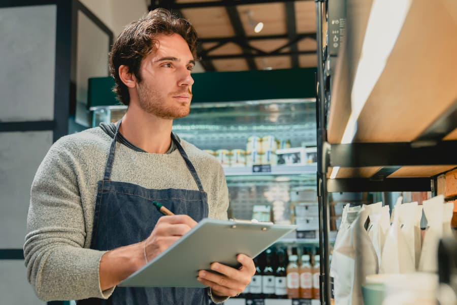 A young man with a clipboard taking inventory in a grocery store.