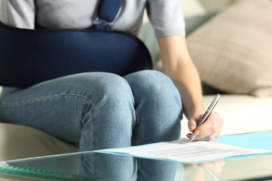 Close-up of a woman with her arm in sling writing on a piece of paper.