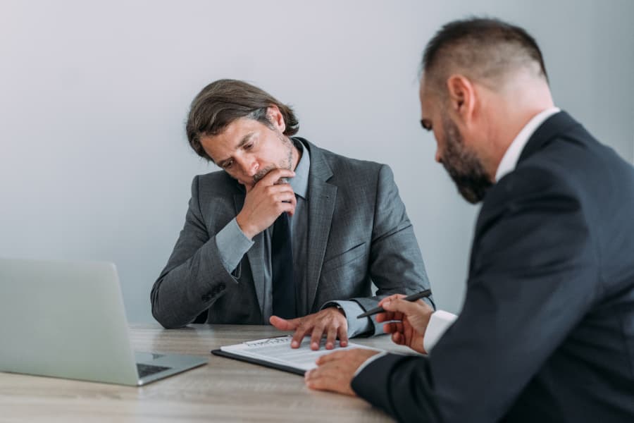 Two men at a table reviewing a document on a clipboard