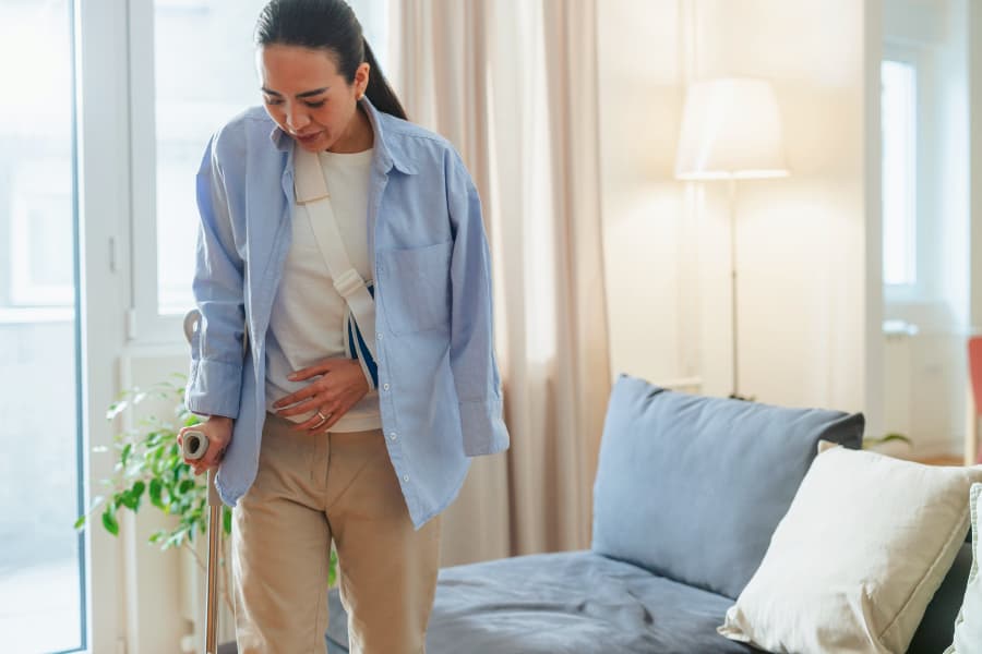 Woman with her arm in a sling using a cane to walk.