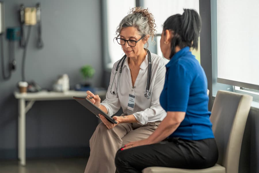 A patient sitting with a female doctor writing on a clipboard.