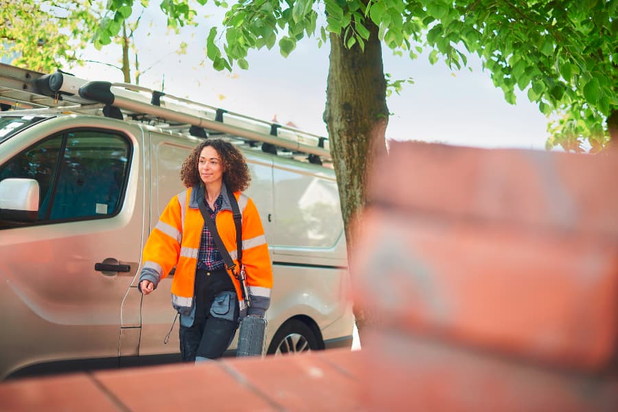 A woman in an orange jacket walking away from a silver van to go to work.